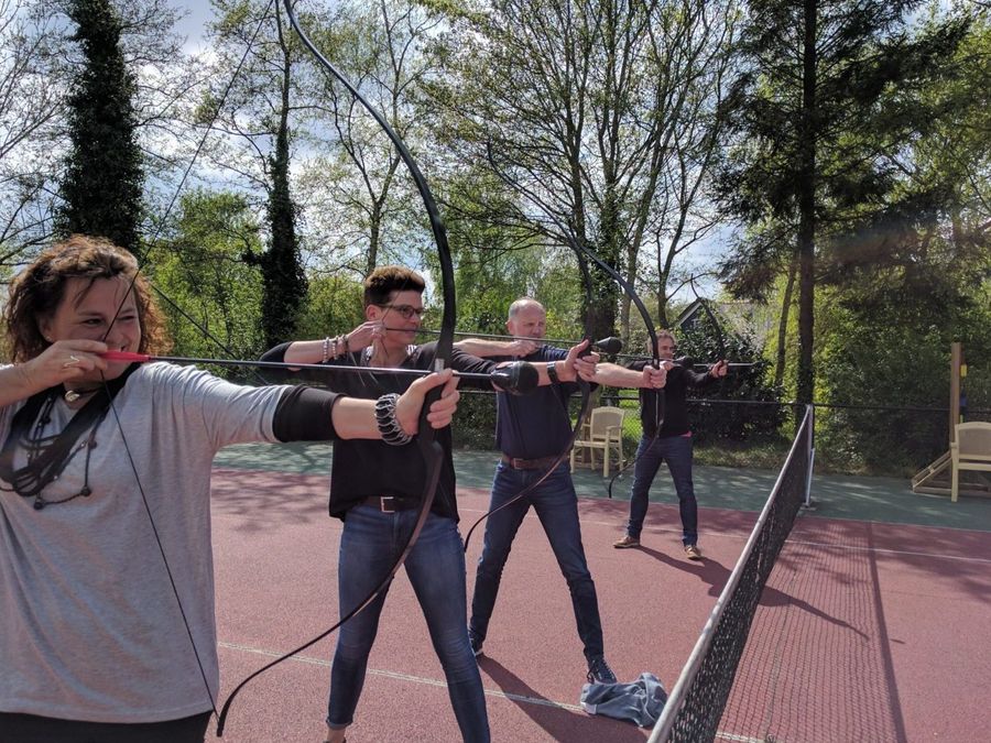 Participants shooting with bow and arrow in a field with wooden targets