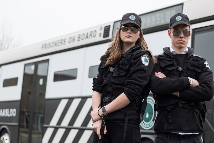 Two guards in black uniforms with sunglasses in front of the prison bus of Prison Break Paasloo