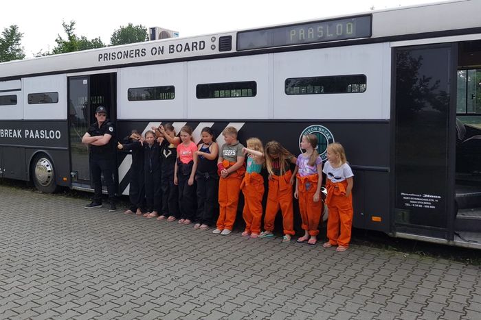 Children in orange overalls and guards in a row in front of the prison bus