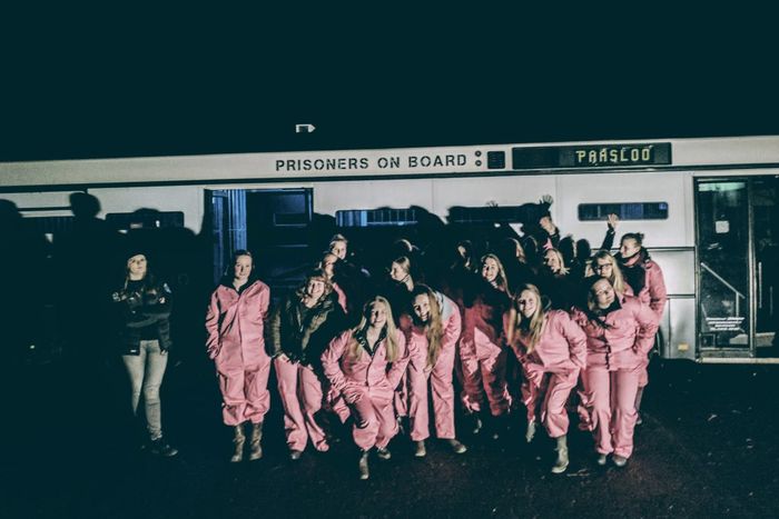 Group of women in pink overalls in front of the prison bus in the evening