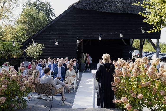 Wedding ceremony outdoors at De Grachthof, with guests on chairs along a white aisle between the hydrangeas