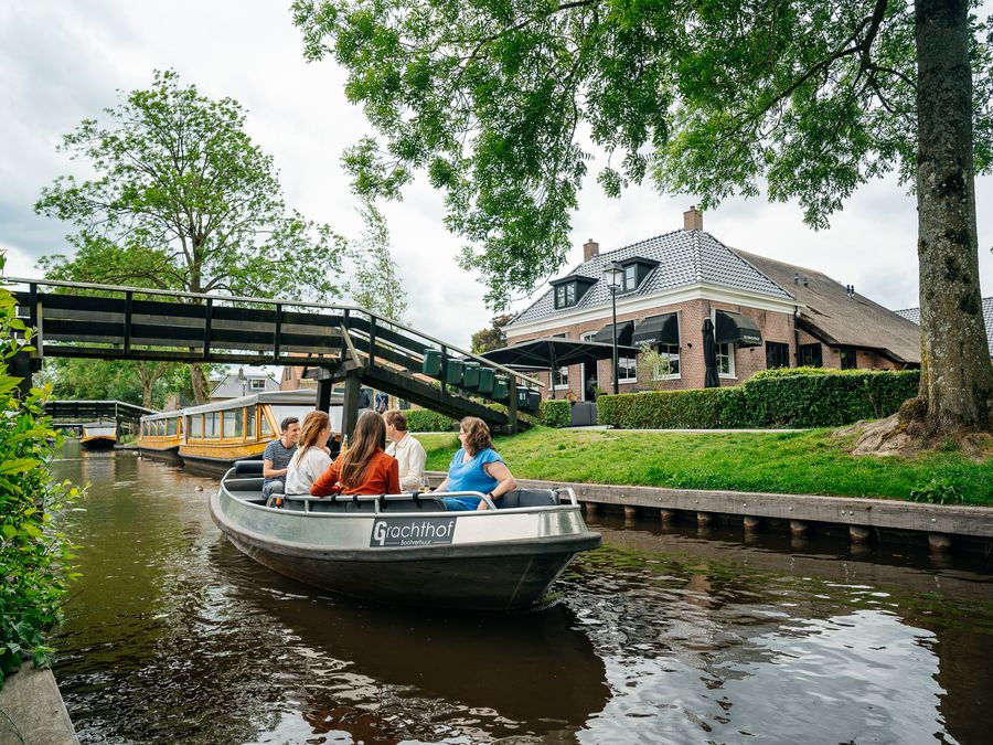 Rental sloop from De Grachthof with a group on board on the canal, with a wooden bridge in the background