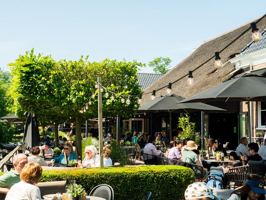 Guests in the sun on the terrace of De Grachthof, with parasols, string lights and a tall hedge