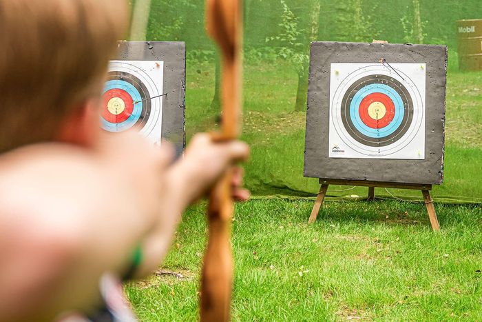 Child with a wooden hand bow aiming at a target in the grass