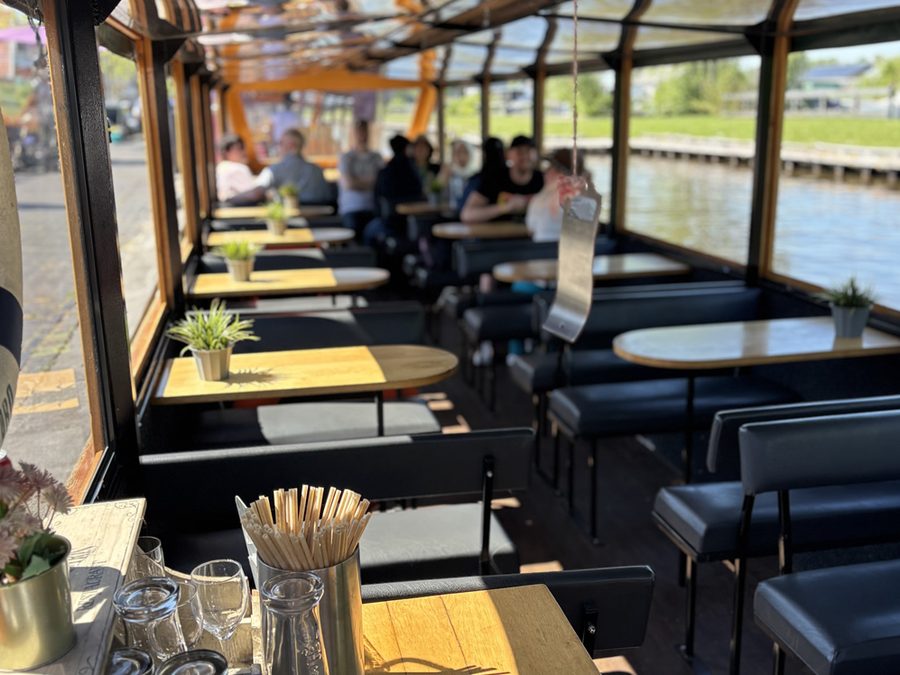 Interior of a covered De Rietstulp tour boat with small tables along the windows