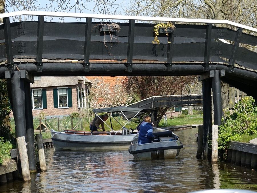Elektroboote fahren unter einer Holzbrücke in einer Gracht in Giethoorn hindurch