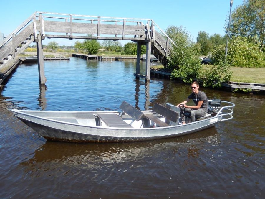 Konsolenboot mit Steuerrad fährt unter einer weißen Fußgängerbrücke in Giethoorn hindurch