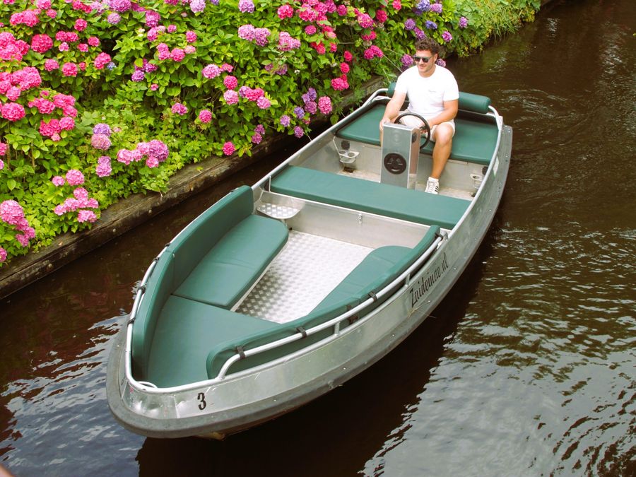 Elektrische Sloep mit grünen Kissen fährt an rosa Hortensien auf einer Gracht vorbei