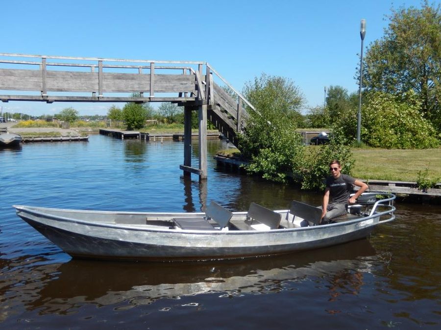 Großes Flüsterboot mit Rückenlehnen fährt unter einer weißen Fußgängerbrücke in Giethoorn hindurch