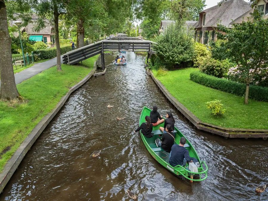 Zwei Personen in einem grünen Flüsterboot auf einer schmalen Gracht in Giethoorn, mit einer kleinen Holzbrücke
