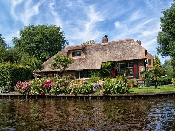 Hof mit Reetdach und blühendem Garten an einer Gracht in Giethoorn
