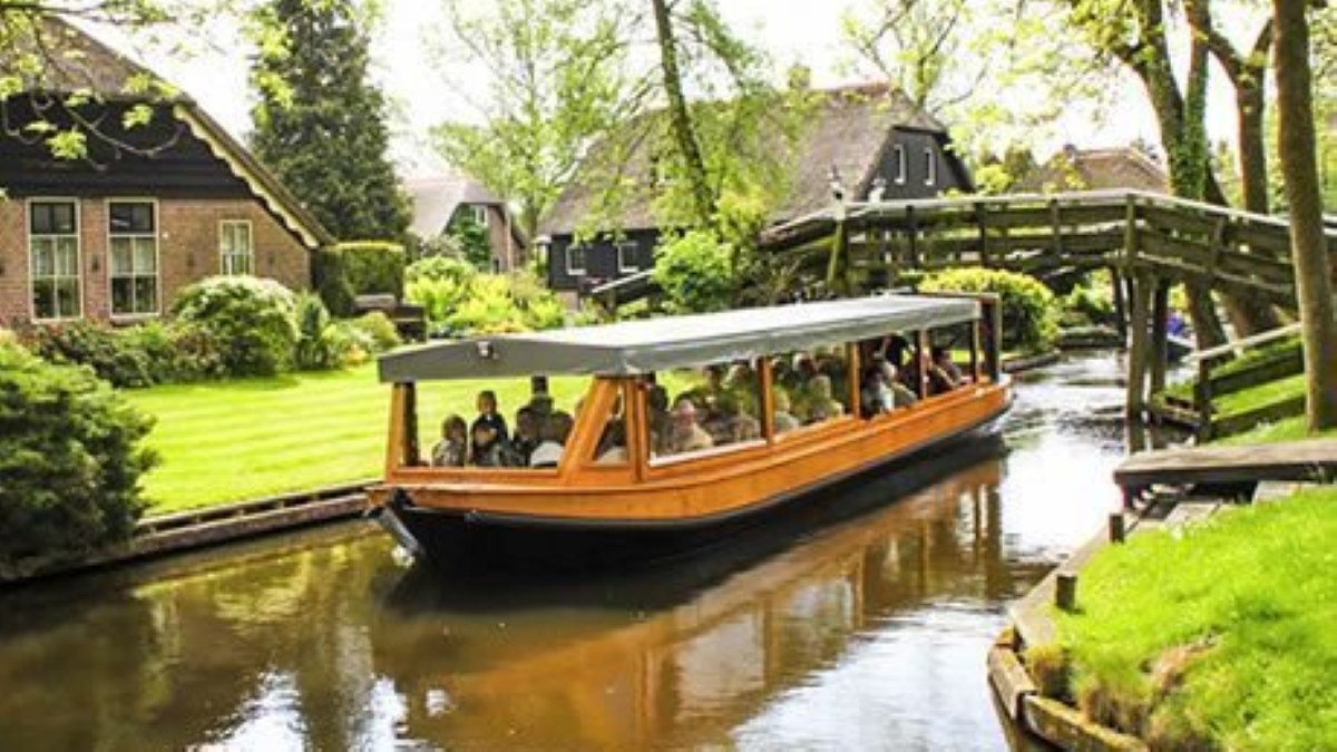 Überdachtes Rundfahrtboot mit Fahrgästen auf einer Gracht in Giethoorn, mit einer kleinen Holzbrücke