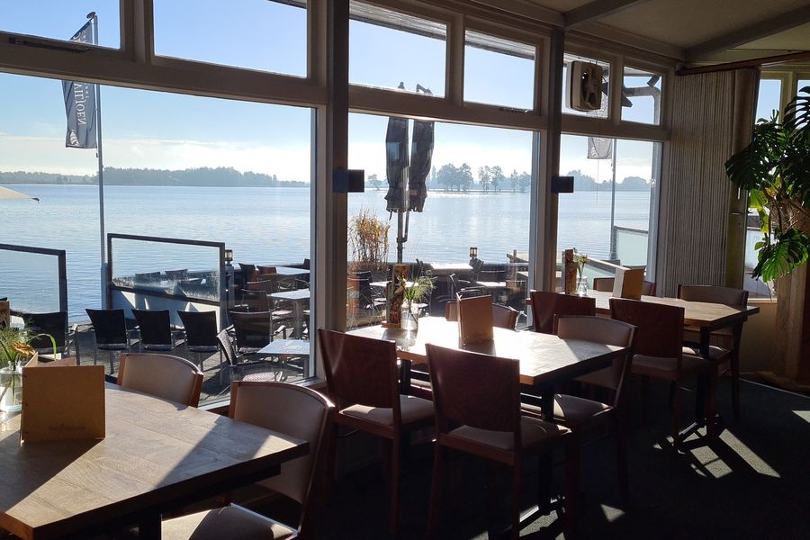 Restaurant von Smit’s Paviljoen mit Tischen an den großen Fenstern und Blick über den See