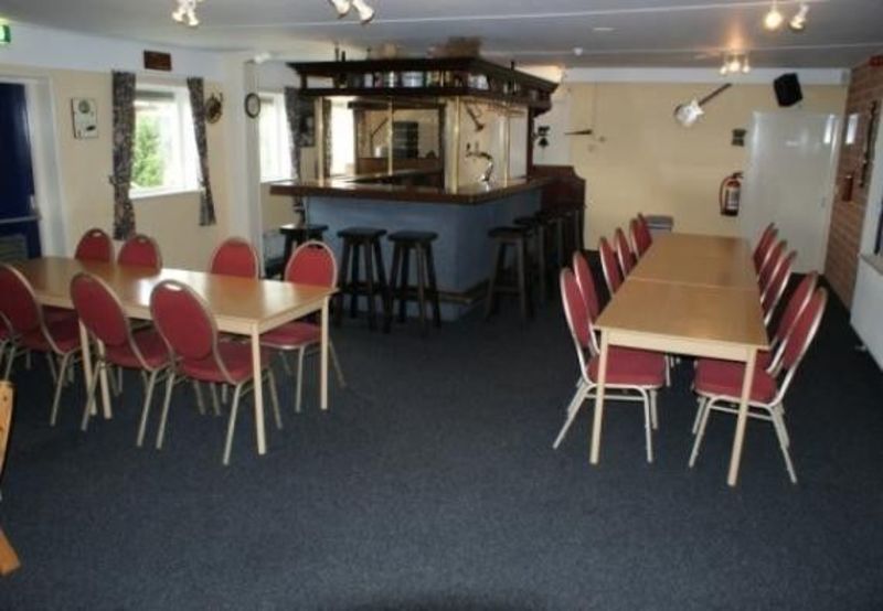Common room of the group accommodation with long tables, red chairs and a bar