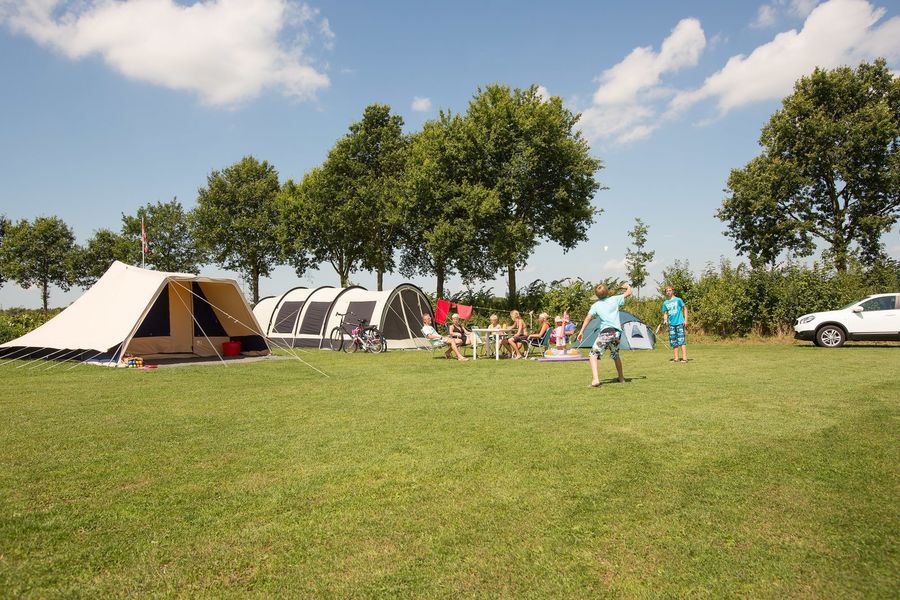 Tents and a caravan on a grass field with trees at the campsite in Vollenhove