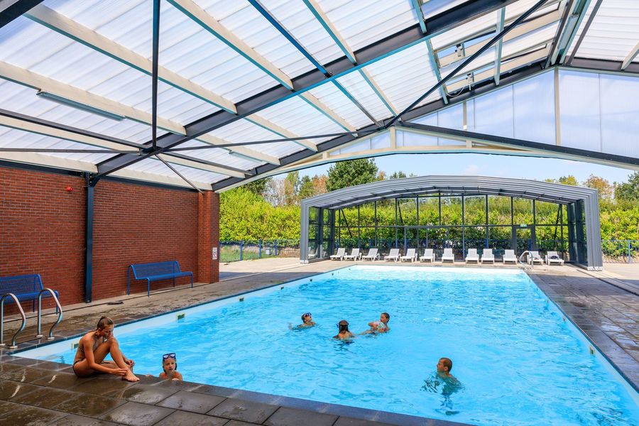Covered swimming pool of Vakantiepark 't Akkertien with open sliding roof and swimming guests