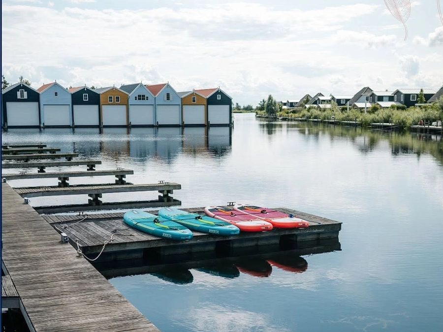 Harbour of Villa Bodelaeke with wooden jetties, paddleboards and coloured boathouses on the far side
