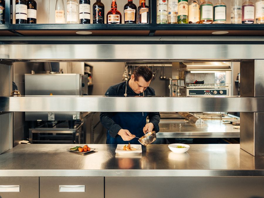 Chef at work in the open kitchen of Villa Bodelaeke, with a row of bottles above