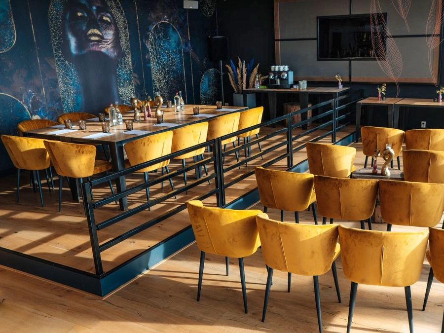 Hall of Villa Bodelaeke with long tables, ochre chairs and a large mural