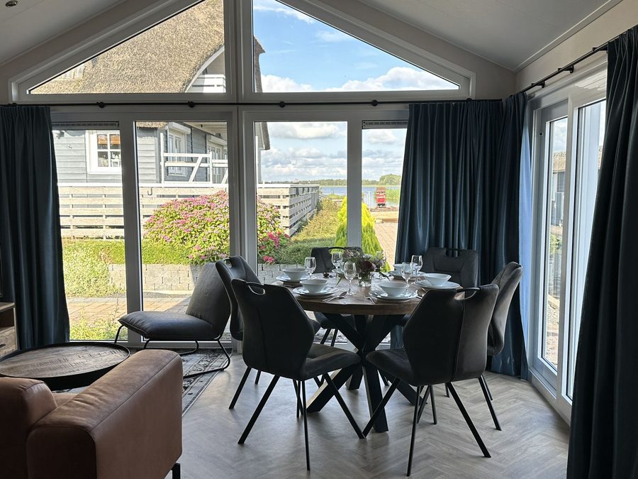 Living room of a chalet with dining table and large windows overlooking the garden and water