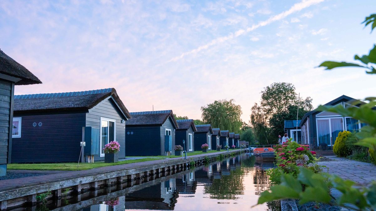 Row of dark chalets along a canal at Waterpark Giethoorn