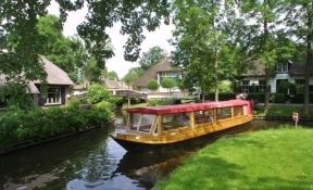 Überdachtes Rundfahrtboot von 't Zwaantje in einer Gracht zwischen den Häusern von Giethoorn