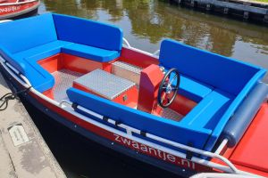 Rotes Mietboot mit blauen Kissen und einem Steuerrad am Steg in Giethoorn