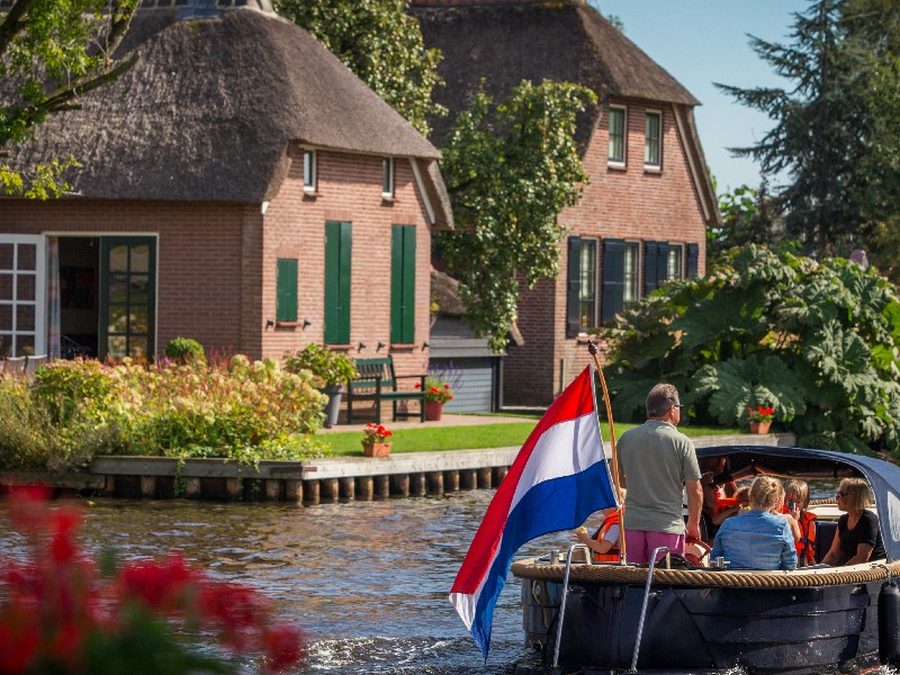 Thatched farmhouses on the water in Giethoorn with a sloop flying the Dutch flag