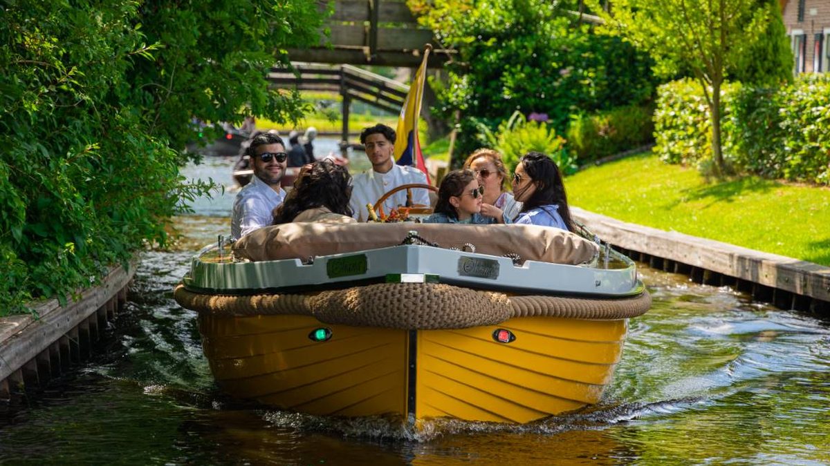 Yellow sloop with skipper and guests sailing along a canal in Giethoorn
